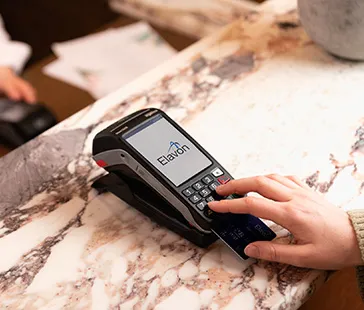 Nahaufnahme einer Person, die eine Kreditkarte in ein Zahlungsterminal auf einer Marmorarbeitsplatte mit Elavon-Logo einführt.