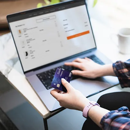 Person nutzt einen Laptop, um einen Online-Einkauf abzuschließen, und hält dabei eine Kreditkarte, während der Warenkorb auf dem Bildschirm angezeigt wird.