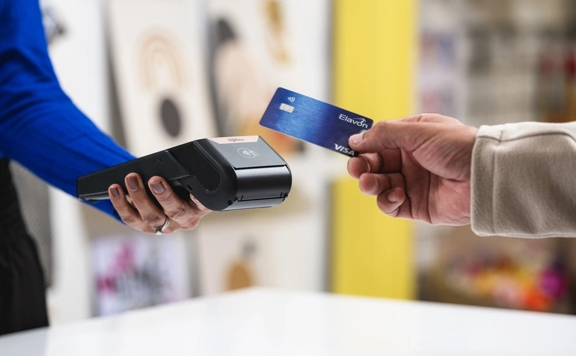 Nahaufnahme einer kontaktlosen kartenzahlung mit einer blauen visa karte und einem kabellosen kartenlesegerät an einer ladentheke