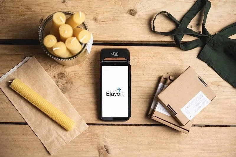 Draufsicht auf ein portables zahlungsterminal auf einem holztisch mit kerzen verpackungen und einer schürze