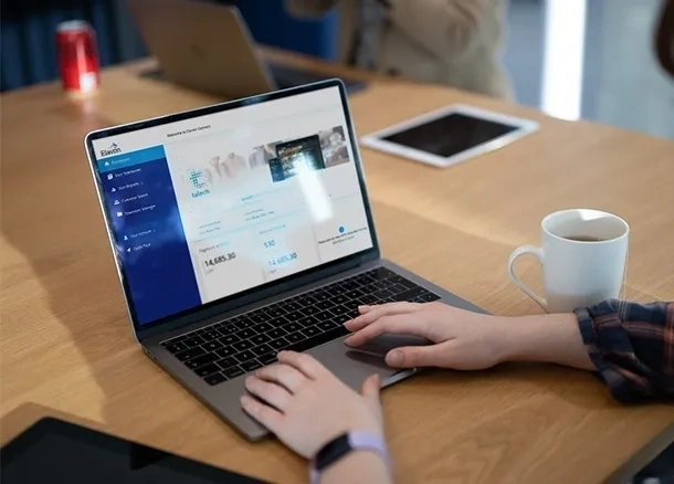 Person nutzt einen laptop auf einem holztisch mit einem kaffeebecher und einem tablet im hintergrund