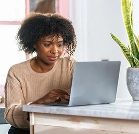 Person nutzt laptop am tisch mit topfpflanze und sonnenlicht durchs fenster