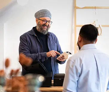Person steht an einem tresen und hält ein zahlungsterminal während sie einem kunden gegenübersteht