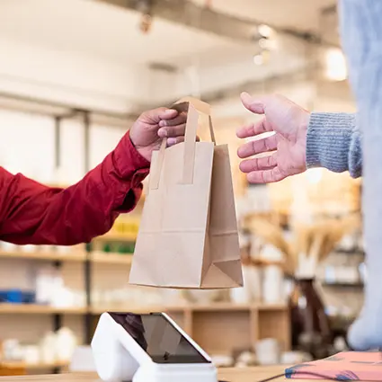 Person übergibt eine papiertüte an einen kunden über einen tresen mit sichtbarem zahlungsterminal