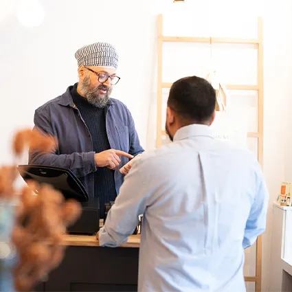 Zwei personen interagieren an einem ladentresen mit kasse und regalen im hintergrund