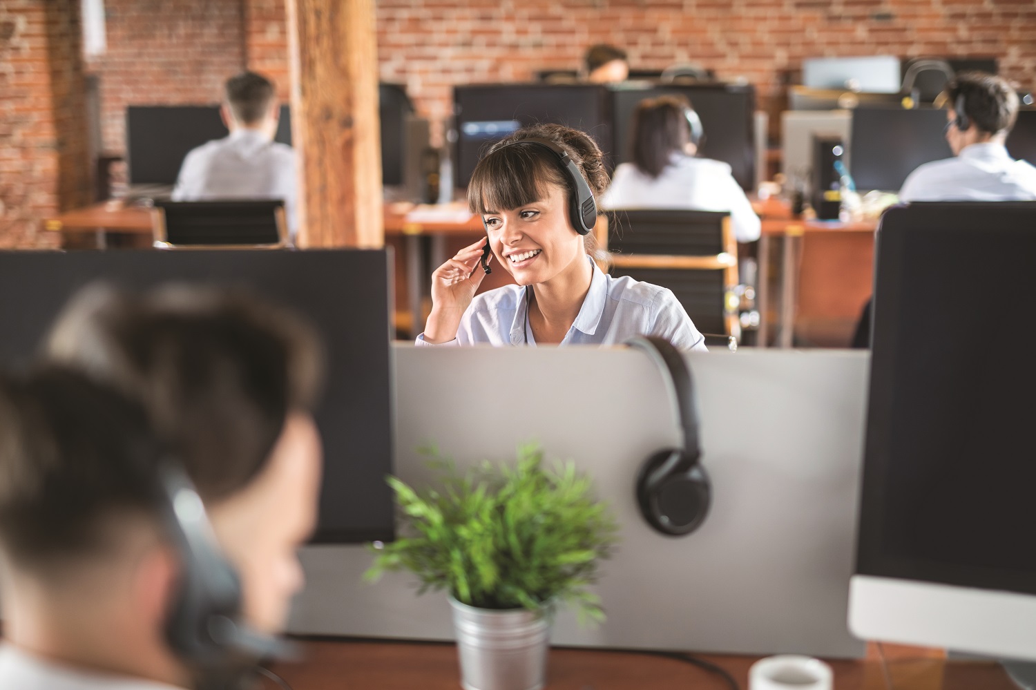 890954530 Call center worker accompanied by her team. Smiling customer support operator at work. Young employee working with a headset.